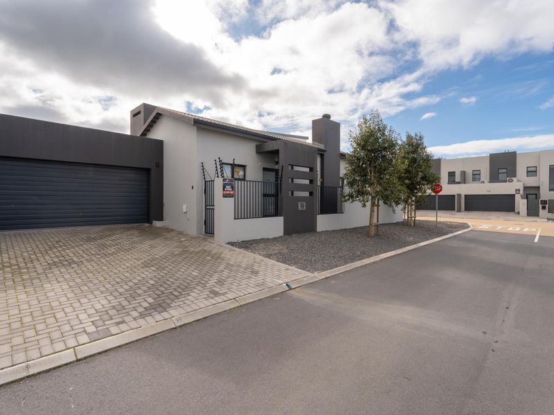 Modern single-story residential property featuring a paved driveway, automated garage, and secure gated entrance with contemporary grey facade finishes.