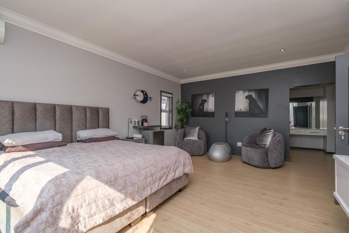 Spacious bedroom featuring light laminate flooring, modern grey accent wall, recessed downlighting, and an integrated air conditioning unit.