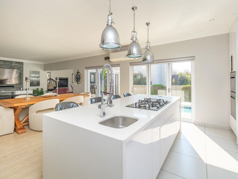 Modern open-plan kitchen and living area featuring a large central island with gas hob, sleek cabinetry, and direct access to the outdoor patio.