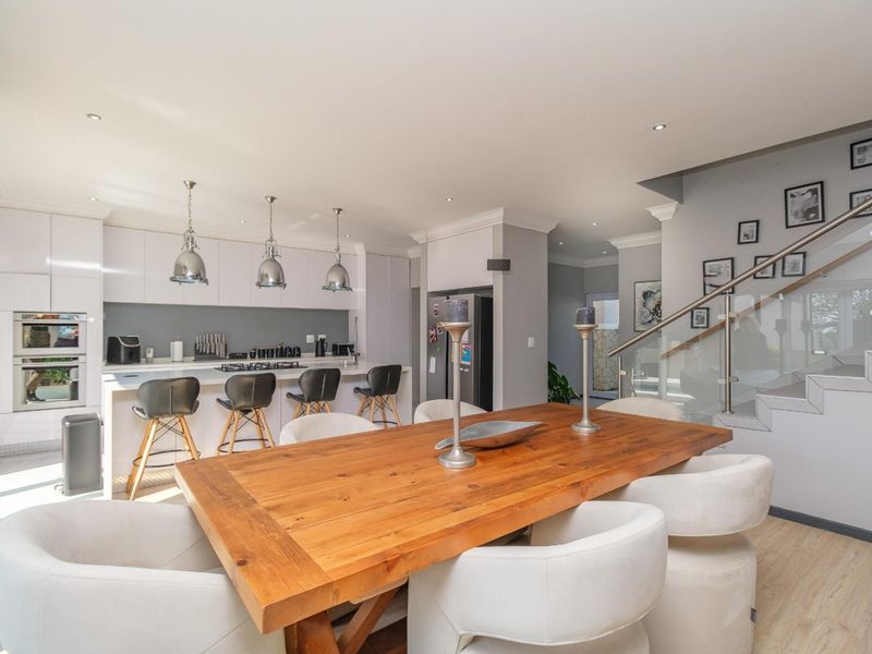 Modern open-plan kitchen and dining area featuring sleek white cabinetry, stone countertops, integrated appliances, and a contemporary staircase with glass balustrades.