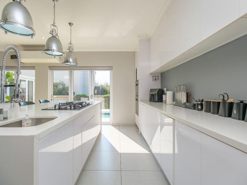 Modern kitchen featuring high-gloss cabinetry, stone countertops, a central island with a gas hob, and sleek pendant lighting, opening to an outdoor area.