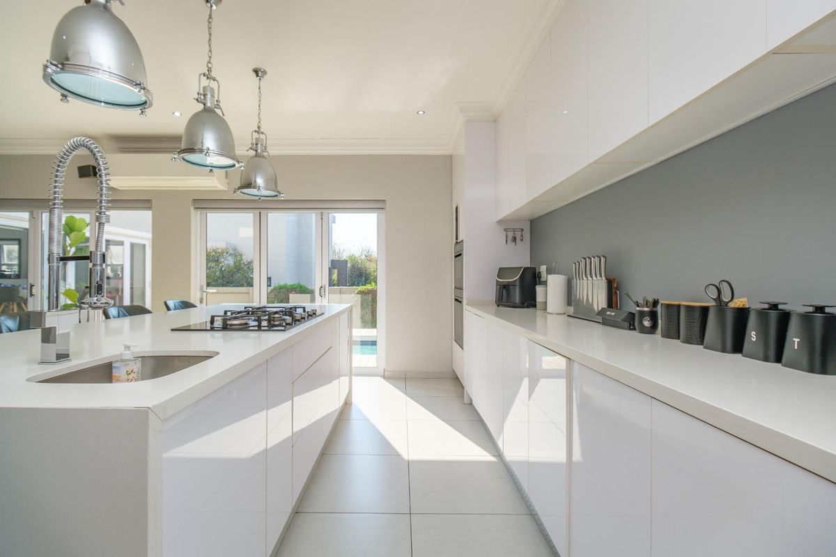 Modern kitchen featuring high-gloss cabinetry, stone countertops, a central island with a gas hob, and sleek pendant lighting, opening to an outdoor area.
