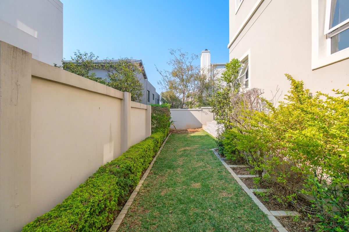 A narrow, well-maintained rear garden area featuring a manicured lawn, established hedge, and boundary wall along the side of the property.