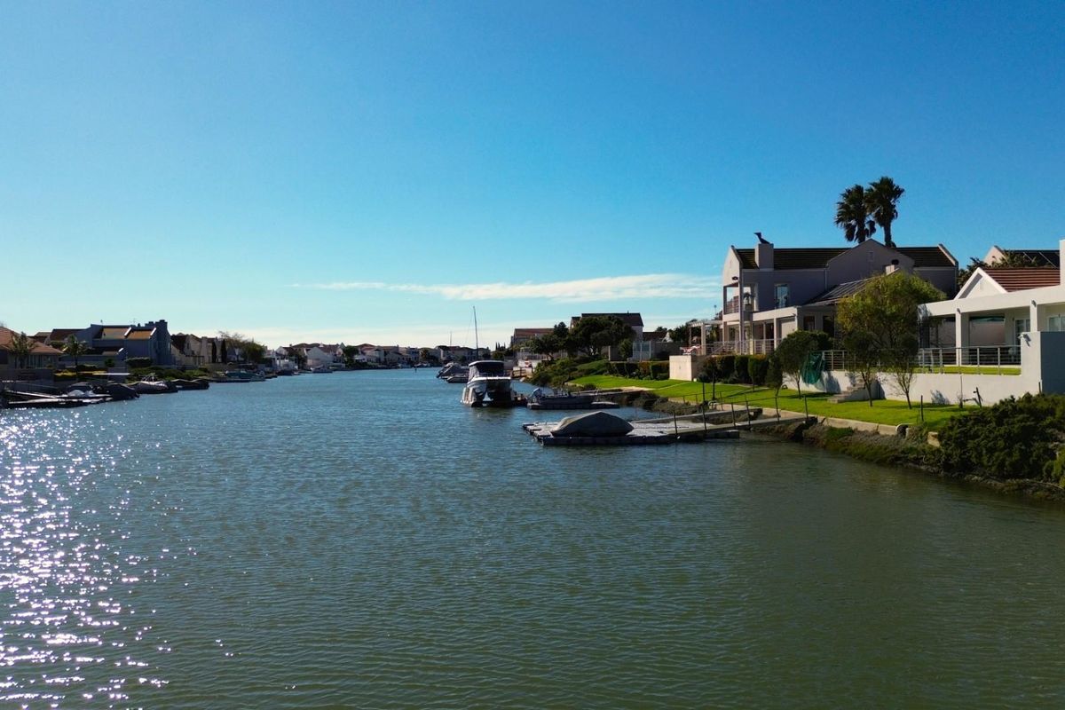 A scenic view of the residential canal and waterfront properties, featuring private jetties and well-maintained landscaped gardens along the water's edge.