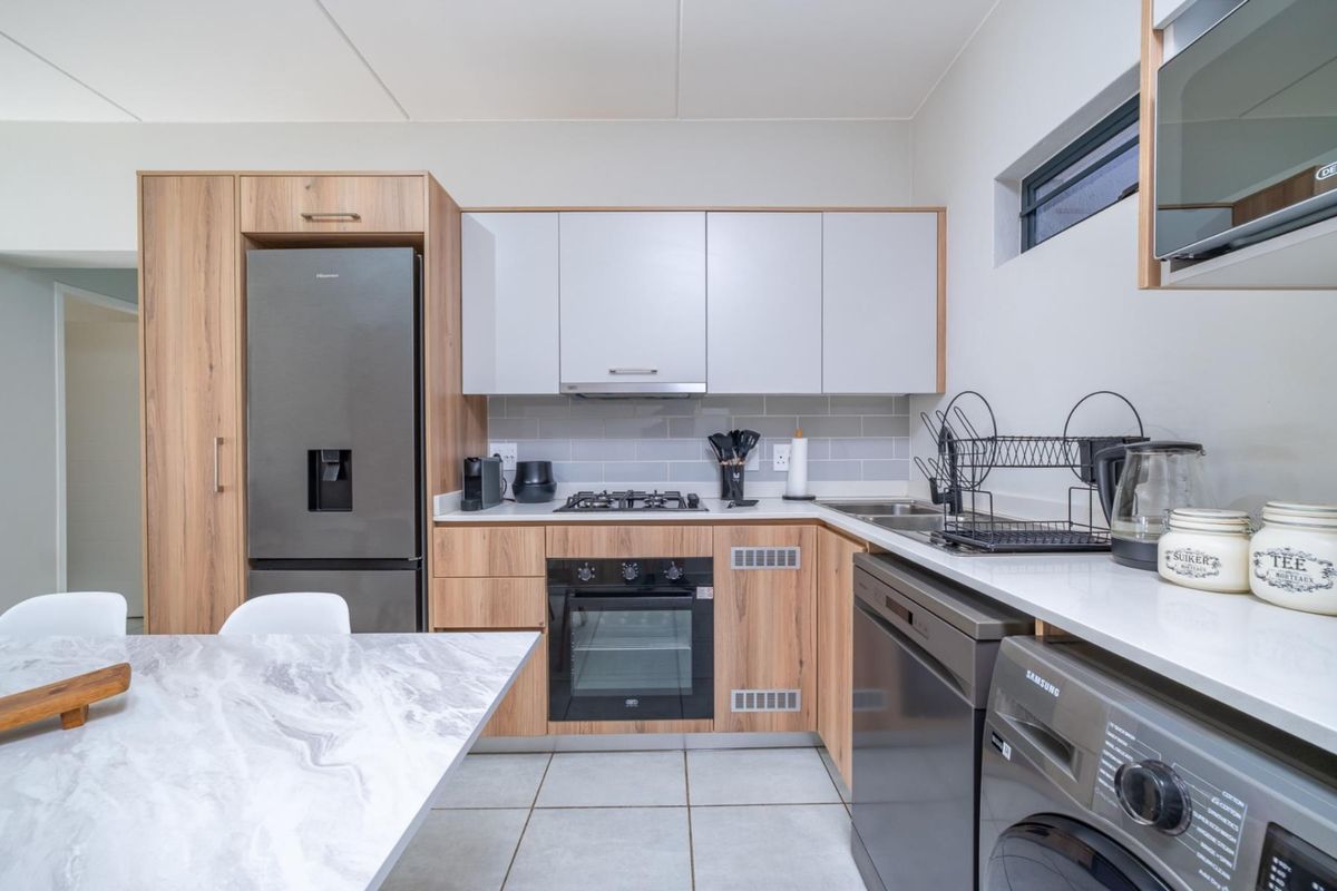 Modern kitchen featuring wood-grain and white cabinetry, stone countertops, gas hob, built-in oven, and tiled backsplash with integrated appliance spaces.