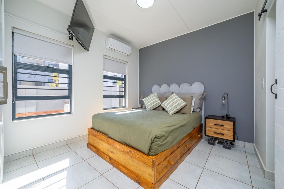 A well-maintained bedroom featuring tiled flooring, an accent wall, air conditioning, and large windows with roller blinds.