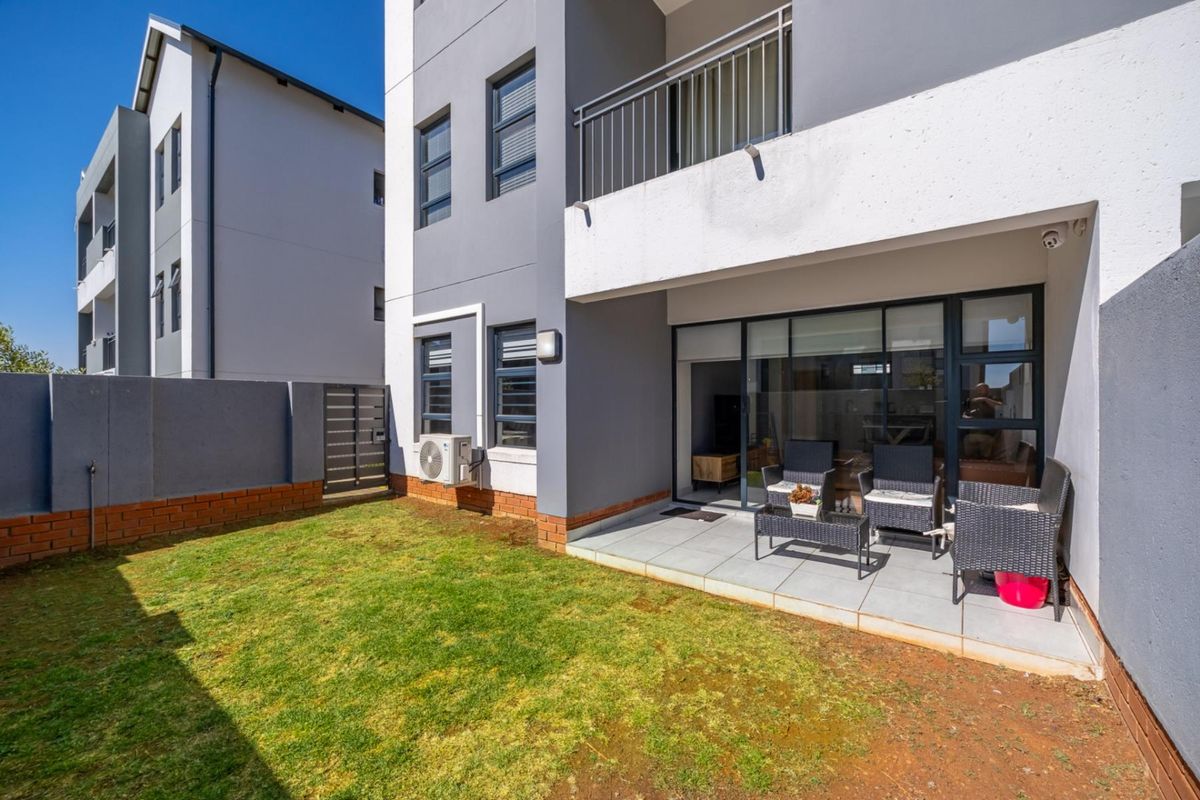Rear view of the apartment featuring a private tiled patio, small garden area, and sliding glass doors leading into the living space.