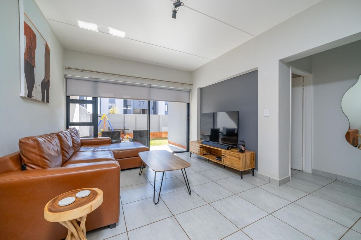 Modern living room featuring large format floor tiles, a feature accent wall, and a wide sliding glass door providing access to the outdoor area.