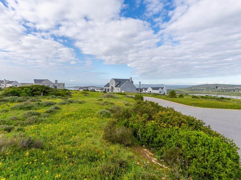 A view of a vacant residential plot featuring native vegetation and access to a paved road within a coastal estate setting.