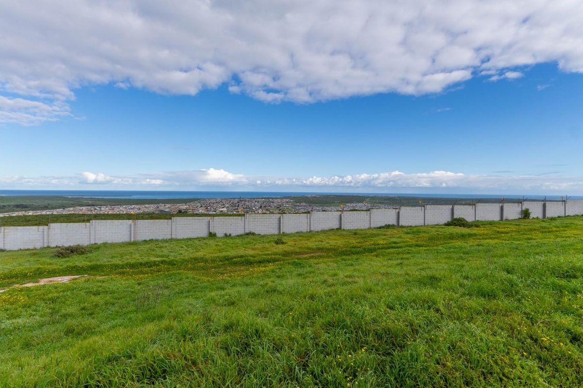 A wide-angle view of the vacant land featuring a perimeter wall and security fencing, overlooking the surrounding landscape and distant coastline.