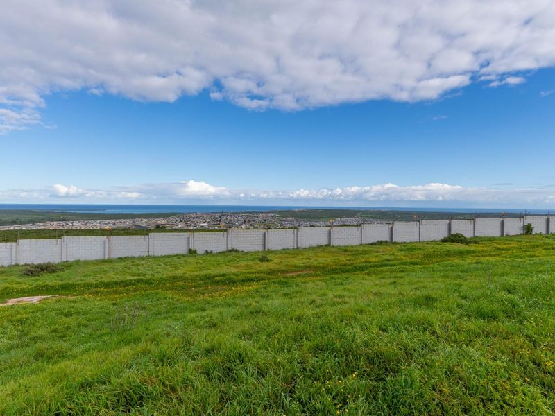 A wide-angle view of the vacant land featuring a perimeter wall and security fencing, overlooking the surrounding landscape and distant coastline.