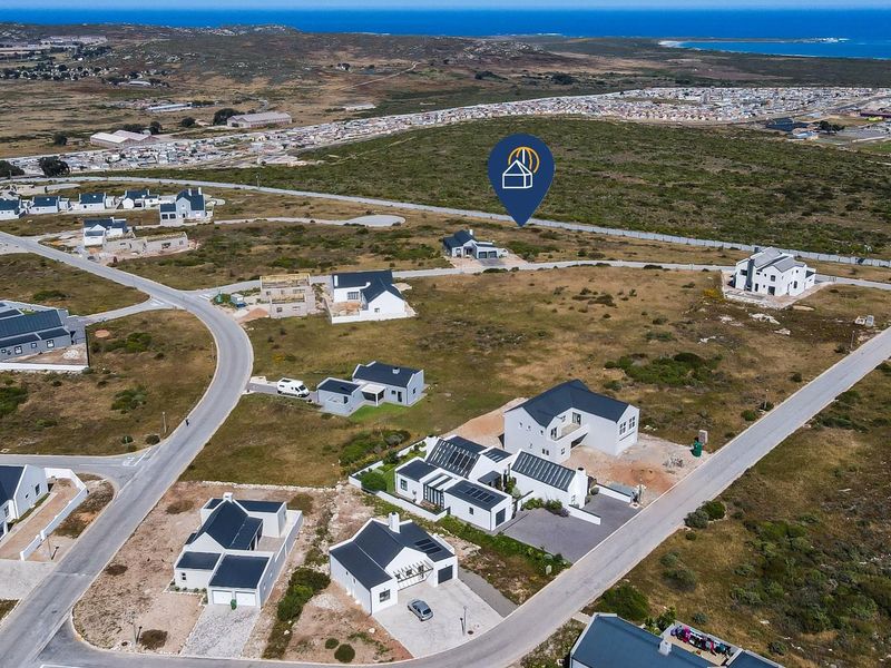 Aerial view of a residential development area featuring vacant plots and established modern homes with coastal surroundings.