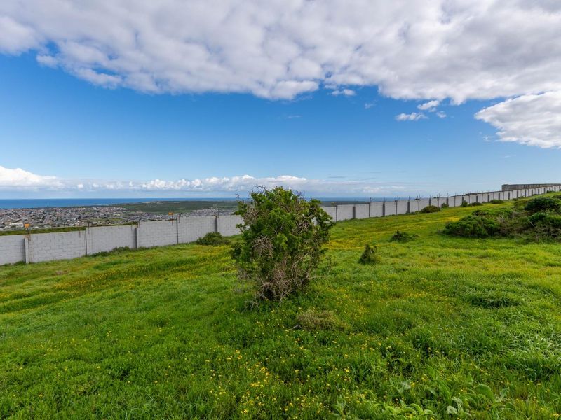 A wide-angle view of a vacant residential plot featuring a perimeter wall with security fencing and distant coastal landscape views.