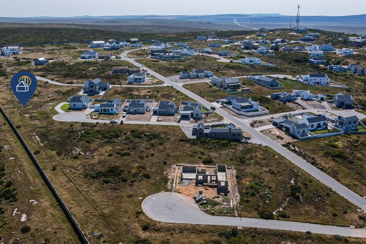 Aerial view of a residential estate featuring paved roads, established homes, and vacant plots with building foundations in a coastal landscape.