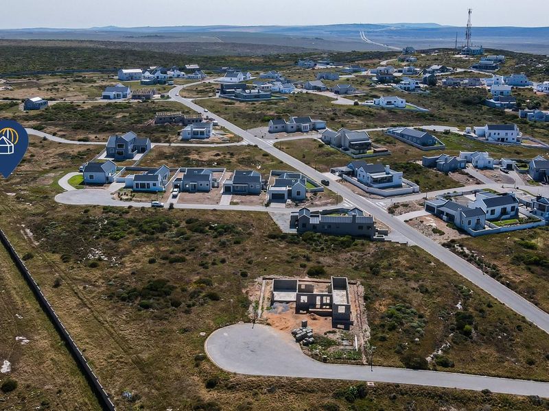 Aerial view of a residential estate featuring paved roads, established homes, and vacant plots with building foundations in a coastal landscape.