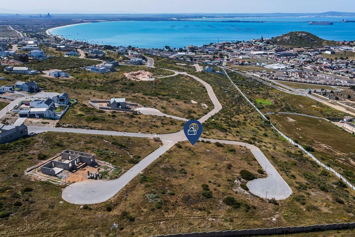 Aerial view of a vacant residential land plot in a coastal development, featuring paved road access and proximity to the ocean.