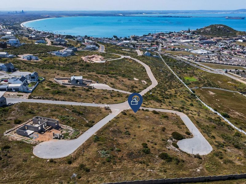 Aerial view of a vacant residential land plot in a coastal development, featuring paved road access and proximity to the ocean.