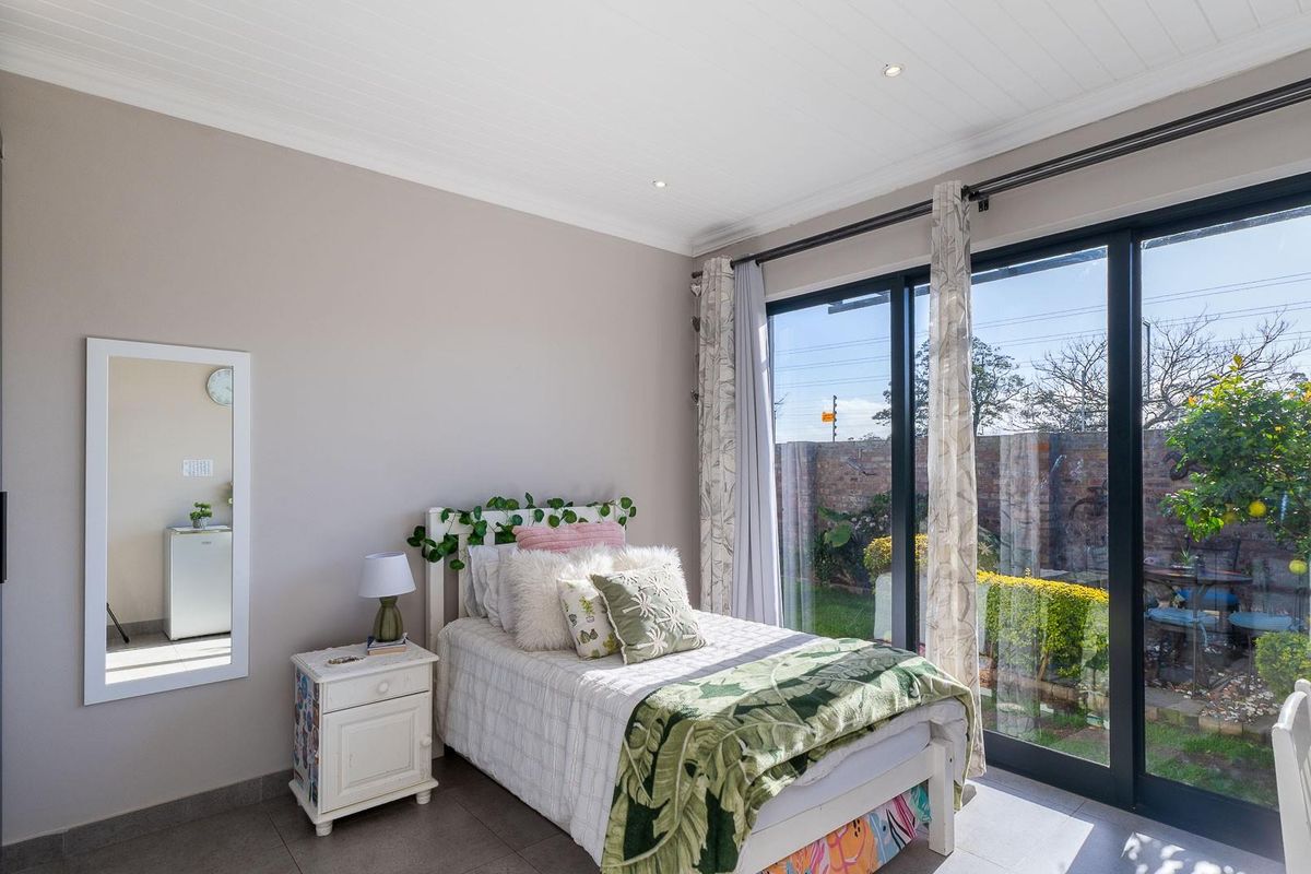 A bright bedroom featuring built-in cupboards, tiled flooring, and large sliding glass doors that provide direct access to the garden.