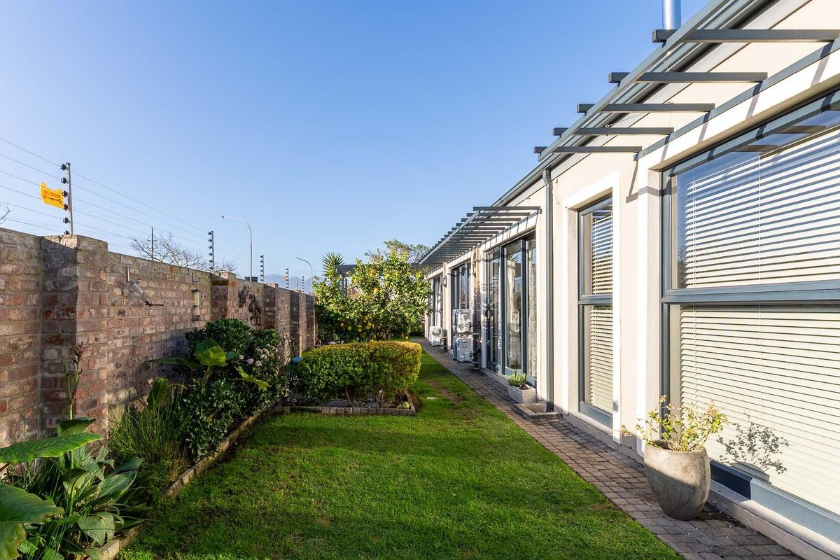 A well-maintained rear garden featuring a manicured lawn, paved walkway, and a brick boundary wall with electric fencing, adjacent to the home's sliding glass doors.