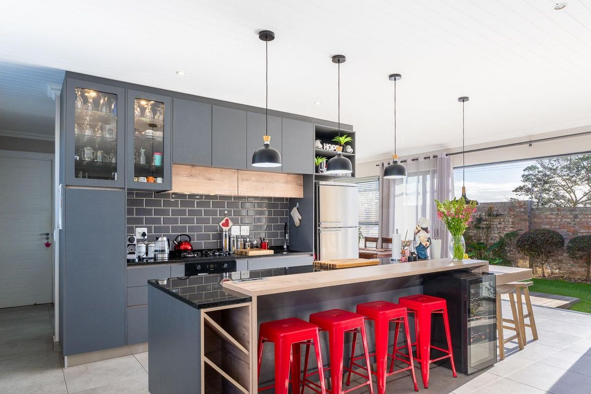 Modern kitchen featuring dark grey cabinetry, stone countertops, subway tile backsplash, and a breakfast bar island with integrated wine cooler, opening to the garden.