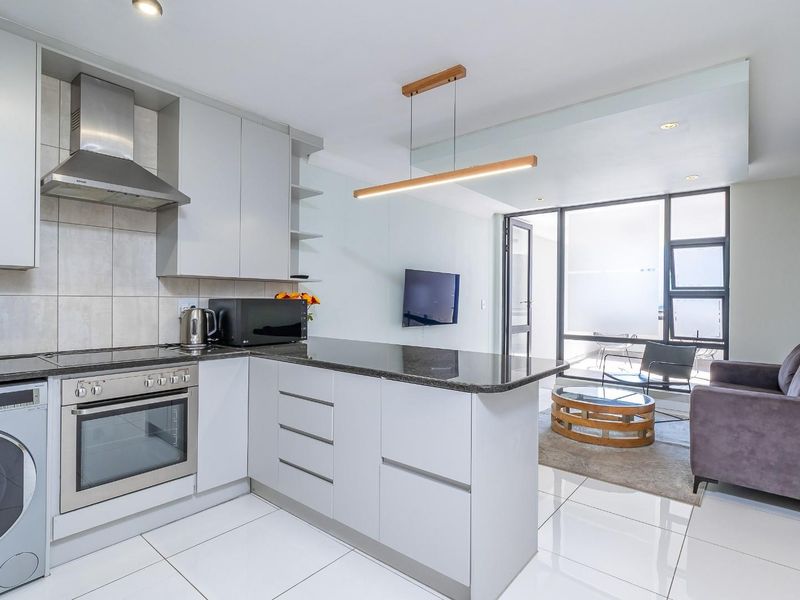 Modern open-plan kitchen and living area featuring sleek cabinetry, granite countertops, integrated appliances, tiled flooring, and direct access to a private balcony.