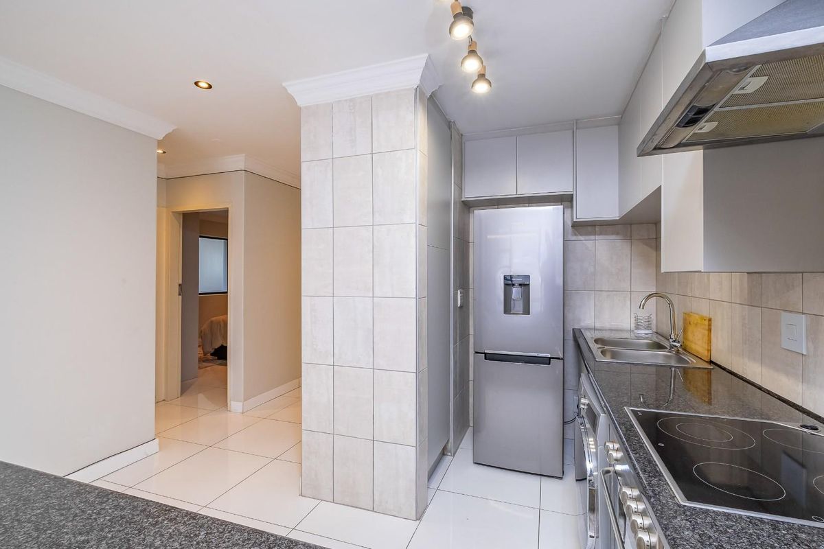 Modern kitchen featuring granite countertops, built-in oven, electric hob, extractor fan, and tiled finishes, leading into a hallway area.