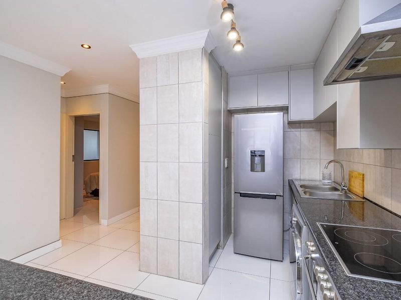Modern kitchen featuring granite countertops, built-in oven, electric hob, extractor fan, and tiled finishes, leading into a hallway area.