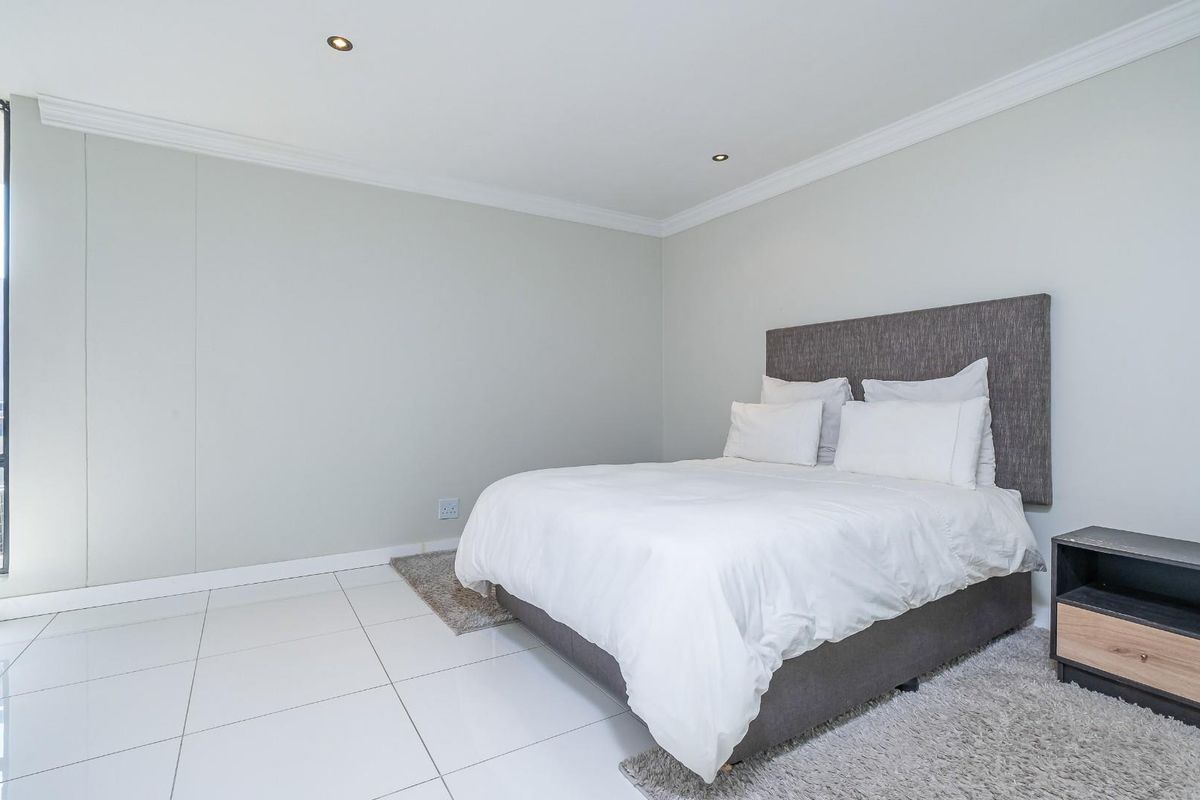 A bright and spacious bedroom featuring neutral walls, modern tiled flooring, recessed downlighting, and large windows allowing for ample natural light.