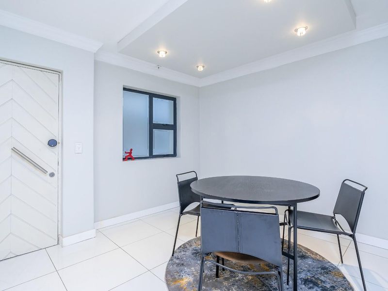 A bright dining area featuring modern tiled flooring, recessed ceiling lighting, and a distinctive chevron-patterned door.