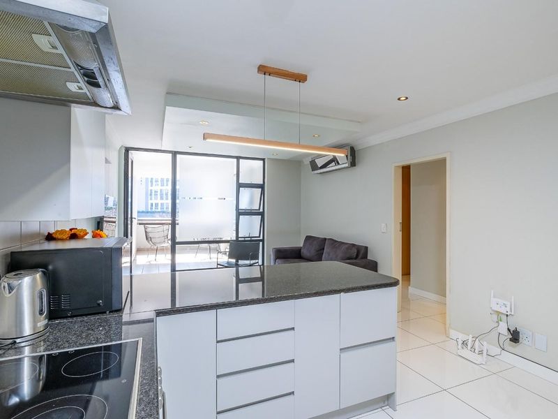 Modern open-plan kitchen and living area featuring granite countertops, sleek cabinetry, tiled flooring, and direct access to a private balcony.