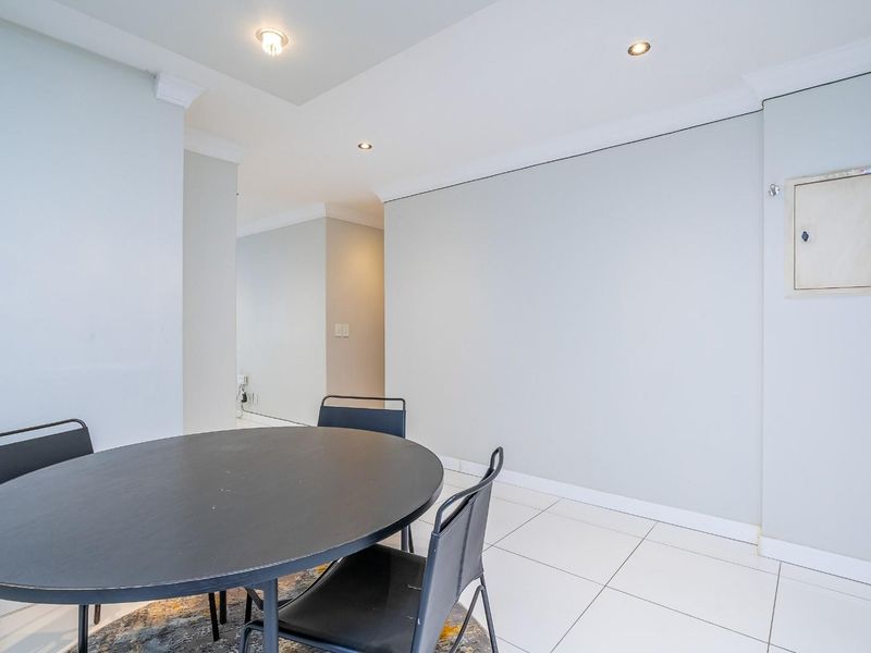A bright, neutral living area featuring clean tiled flooring, recessed downlighting, and coved ceiling details, providing a versatile space for dining or relaxation.