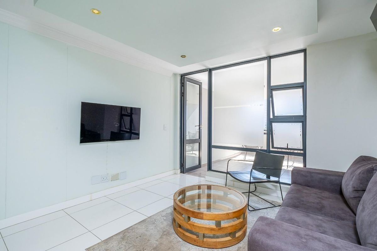 A bright and modern living room featuring tiled floors, recessed lighting, and direct access to an enclosed balcony through large aluminium-framed glass doors.