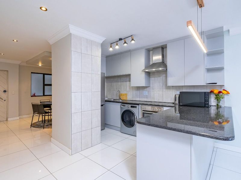 Modern open-plan kitchen featuring sleek cabinetry, granite countertops, integrated appliances, and polished tiled flooring, seamlessly flowing into the adjacent living and dining area.
