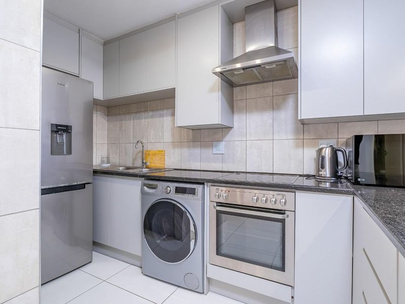 Modern kitchen featuring sleek cabinetry, granite countertops, tiled backsplash, and integrated stainless steel appliances including an oven, hob, and extractor fan.