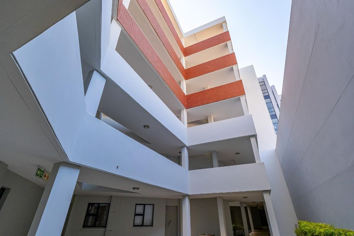 A low-angle view of a modern apartment building facade featuring multi-level balconies, brick accents, and clean white structural finishes.