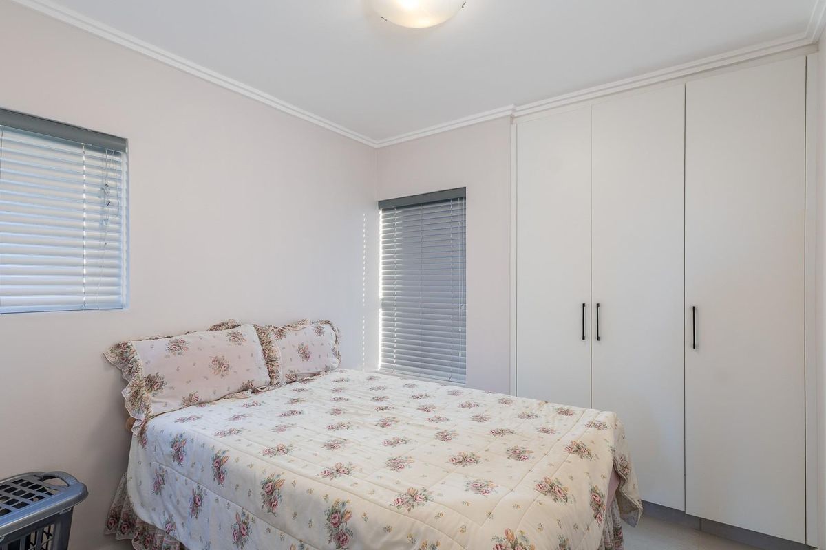 A clean and well-maintained bedroom featuring built-in cupboards, neutral wall finishes, and venetian blinds on the windows.