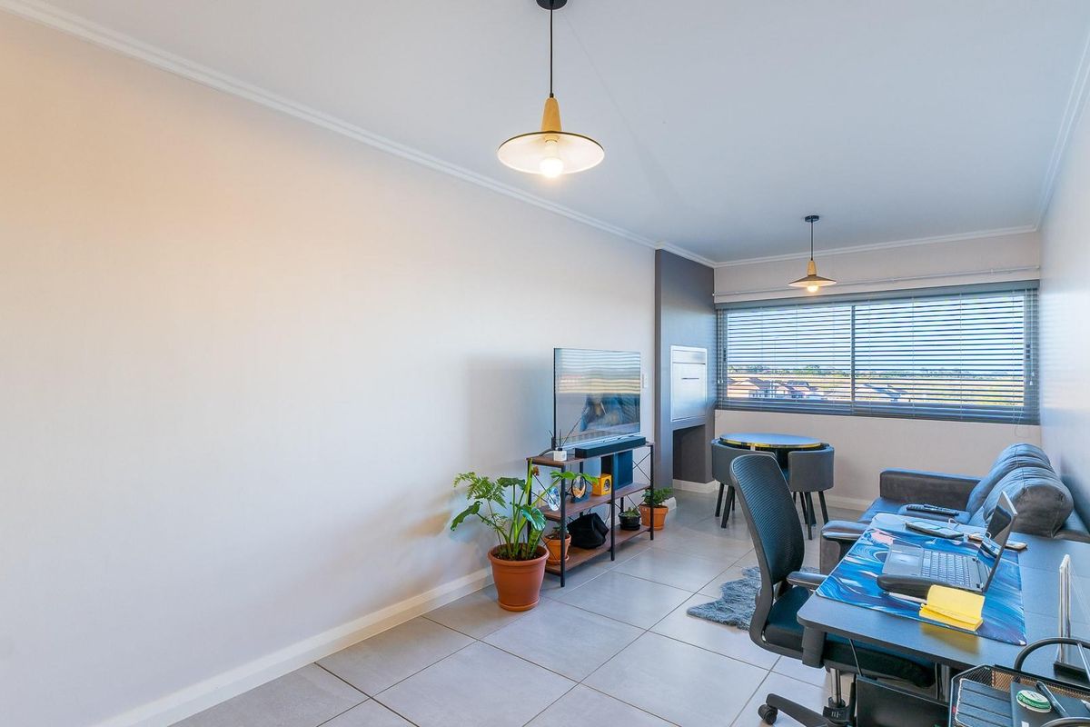 A bright living area featuring neutral tiled flooring, modern pendant lighting, and large windows with venetian blinds offering natural light.