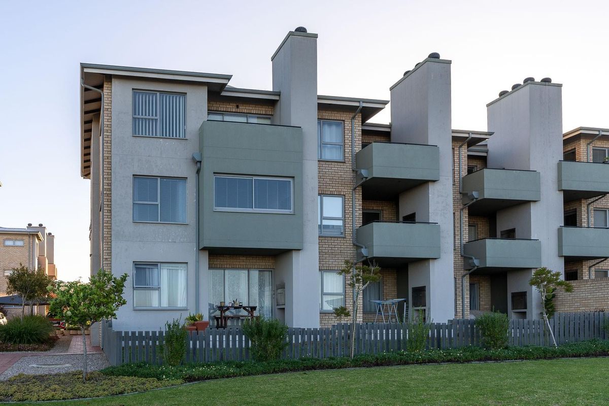 Rear view of a multi-story apartment complex featuring brick facade, private balconies, chimney stacks, and a well-maintained communal garden area.