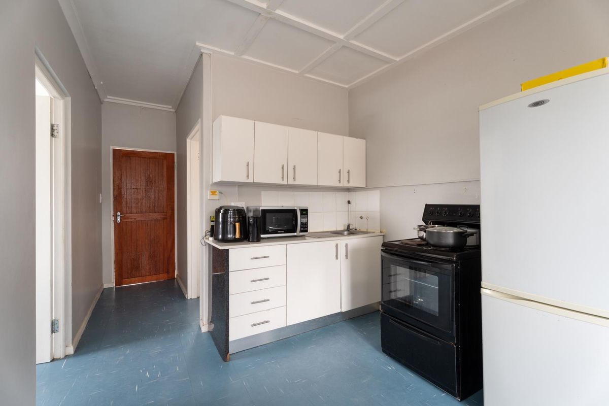A compact kitchen featuring white cabinetry, a stainless steel sink, tiled splashback, and a freestanding oven, with direct access to the hallway.