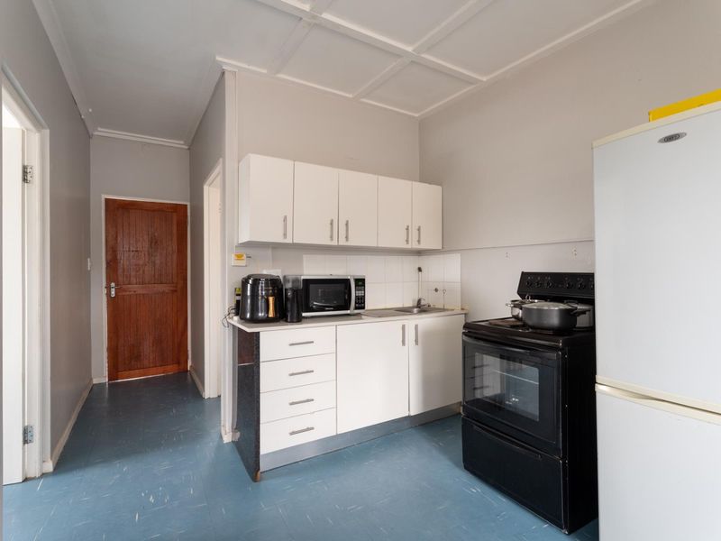 A compact kitchen featuring white cabinetry, a stainless steel sink, tiled splashback, and a freestanding oven, with direct access to the hallway.