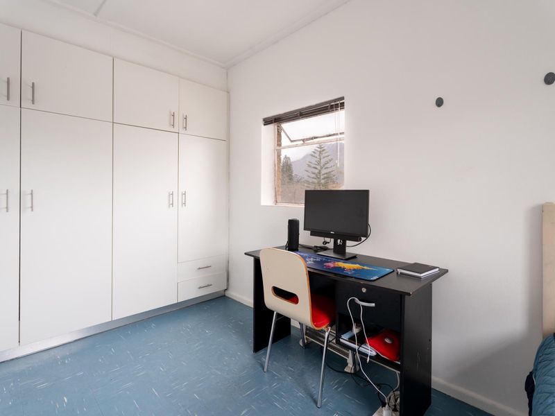 A functional bedroom featuring built-in white cabinetry and a small window, providing a practical space with potential for cosmetic updates.