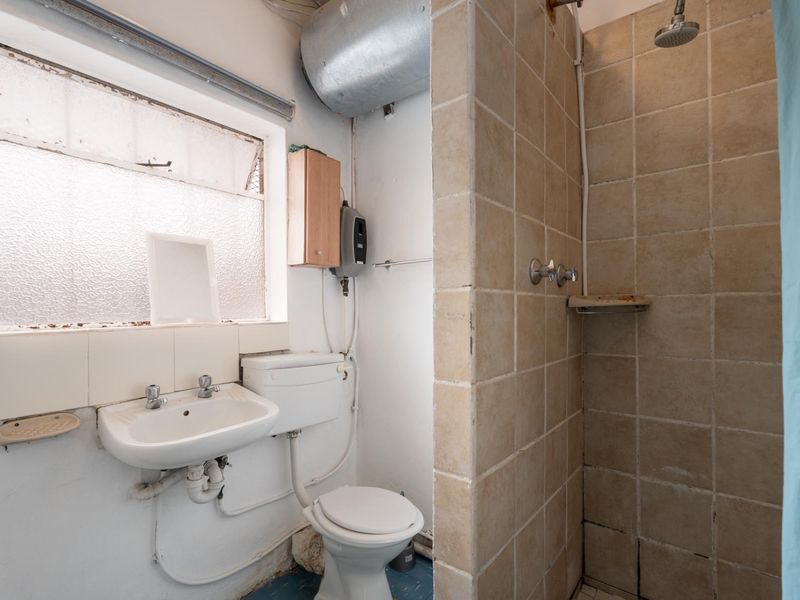 A dated bathroom featuring a tiled shower enclosure, wall-mounted basin, and toilet, requiring significant renovation and modernization of fixtures and finishes.