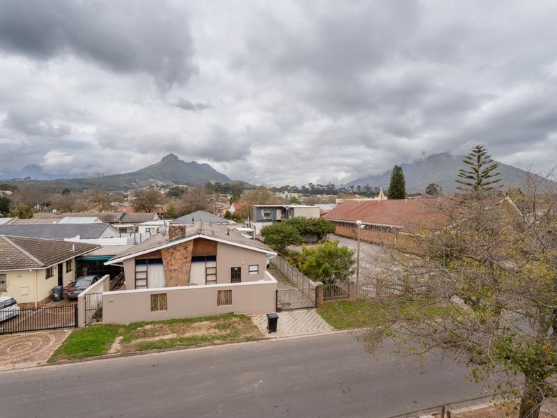 An elevated aerial view of the property showing the building exterior, surrounding neighbourhood, and mountain backdrop.