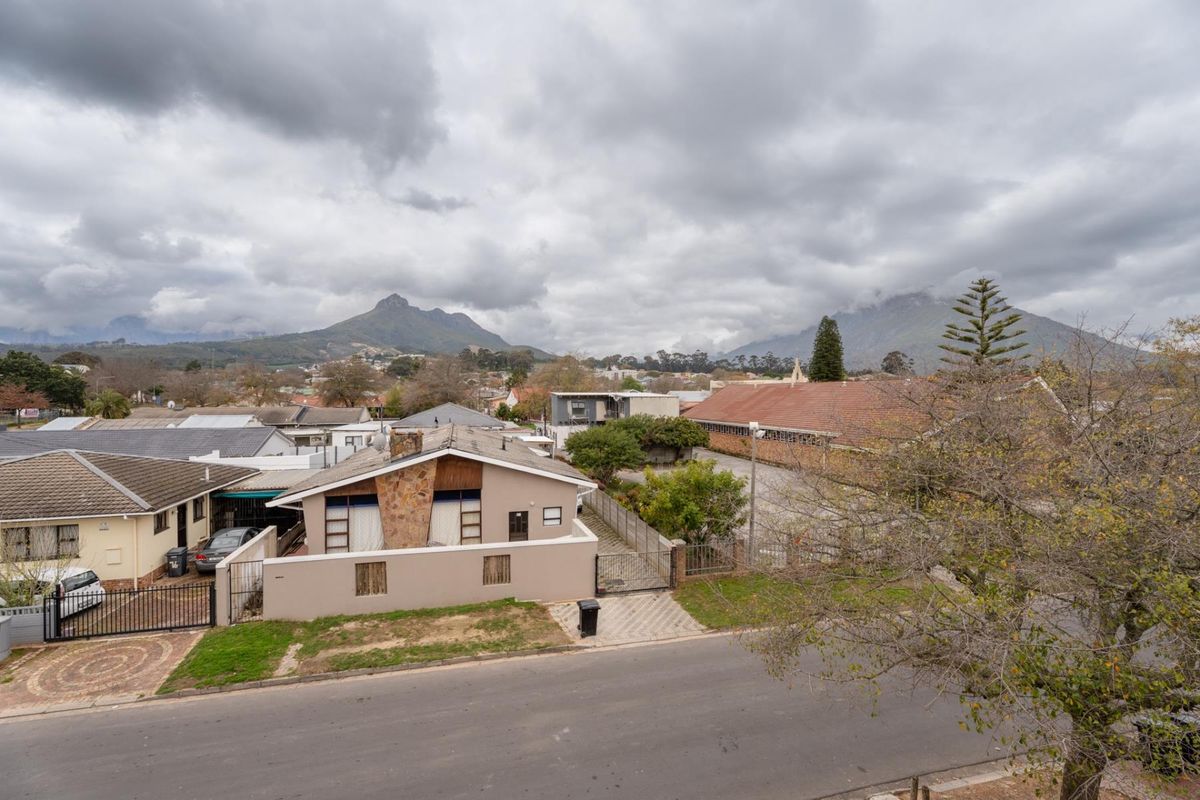 An elevated aerial view of the property showing the building exterior, surrounding neighbourhood, and mountain backdrop.