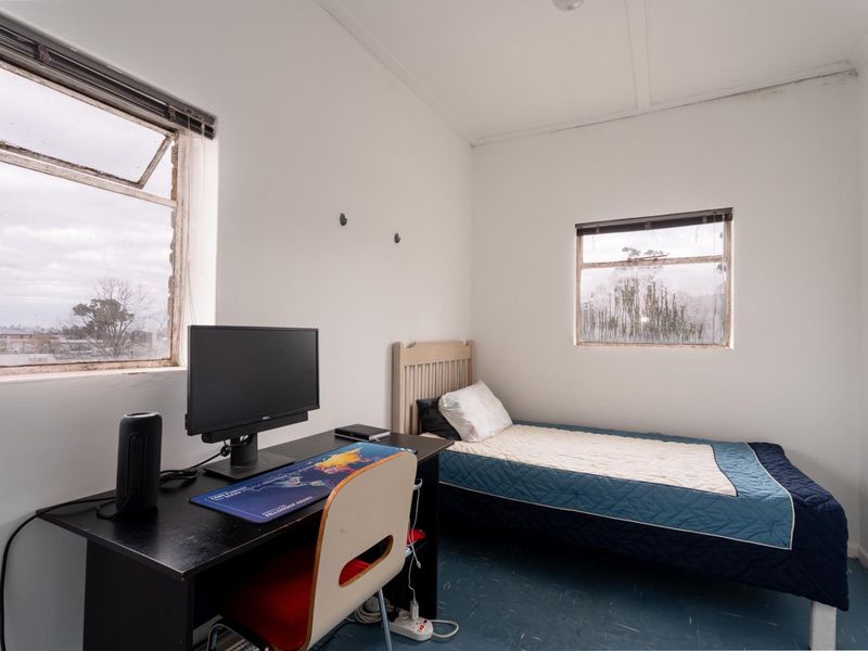 A compact bedroom featuring dual aspect casement windows and vinyl flooring, requiring cosmetic updates to the window frames and general interior finishes.