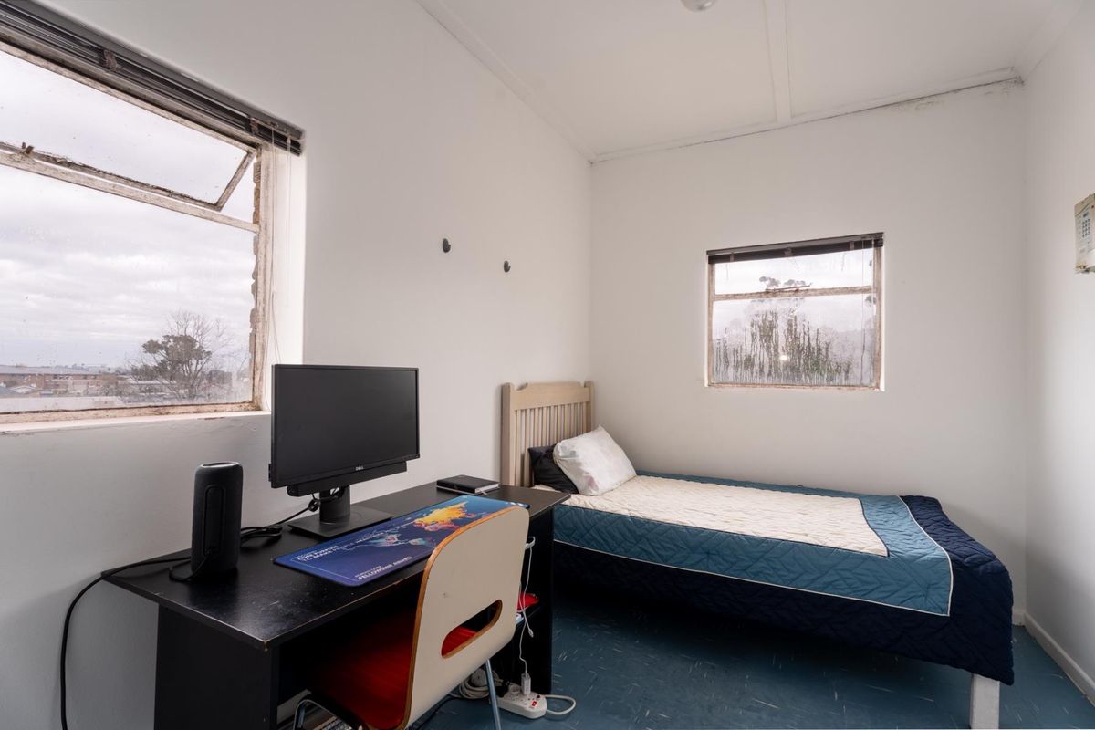 A compact bedroom featuring dual aspect casement windows and vinyl flooring, requiring cosmetic updates to the window frames and general interior finishes.