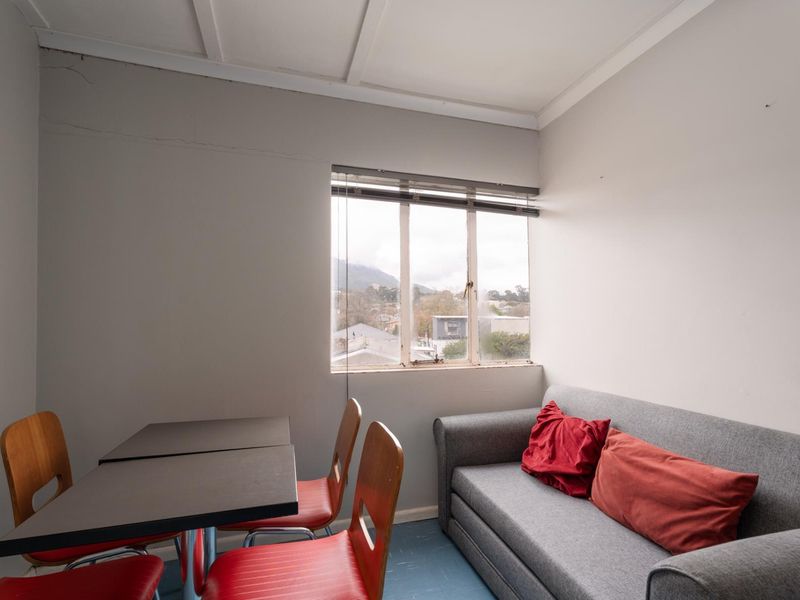 A compact living area featuring a window with views, requiring cosmetic updates to the wall finishes and window frames.