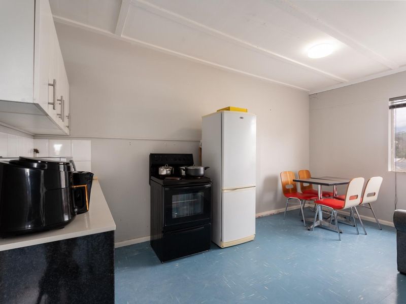 Open plan kitchen and dining area featuring built-in cabinetry, tiled splashback, and a freestanding stove, offering a functional layout with potential for modernization.