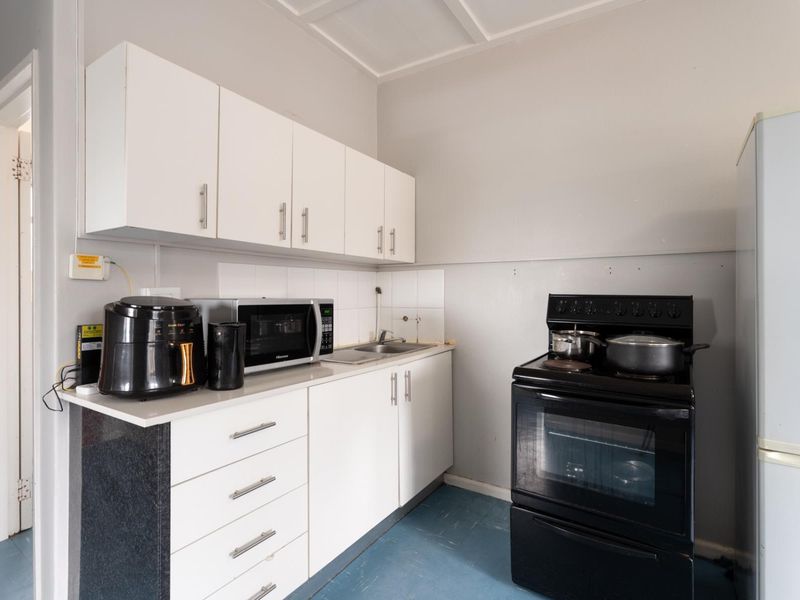 Compact kitchen featuring white cabinetry, laminate countertops, a stainless steel sink, and a freestanding oven, offering a functional layout for a small apartment.