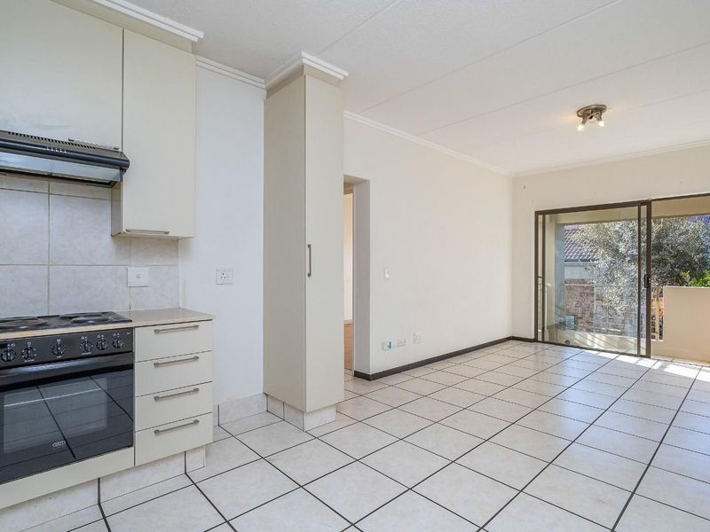 Open-plan kitchen and living area featuring tiled flooring, built-in cabinetry, integrated oven and hob, and sliding glass doors leading to a balcony.